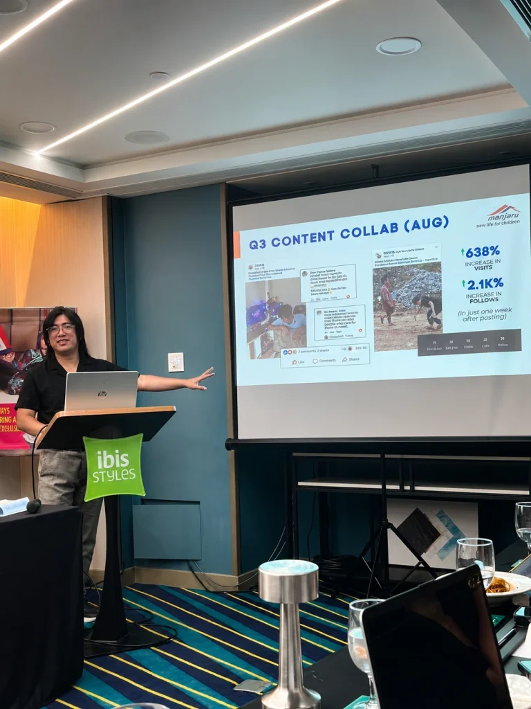 SEO Specialist stands at a podium in a conference room, delivering a presentation beside a large projection screen displaying a Q3 content collaboration performance report. The slide highlights social media campaign results, including increased visits and followers, while attendees listen from their seats.